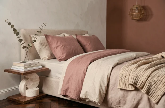 Chambre cocooning avec literie en lin et coton superposés, table de chevet en travertin et mur en badigeon terracotta pour un décor raffiné